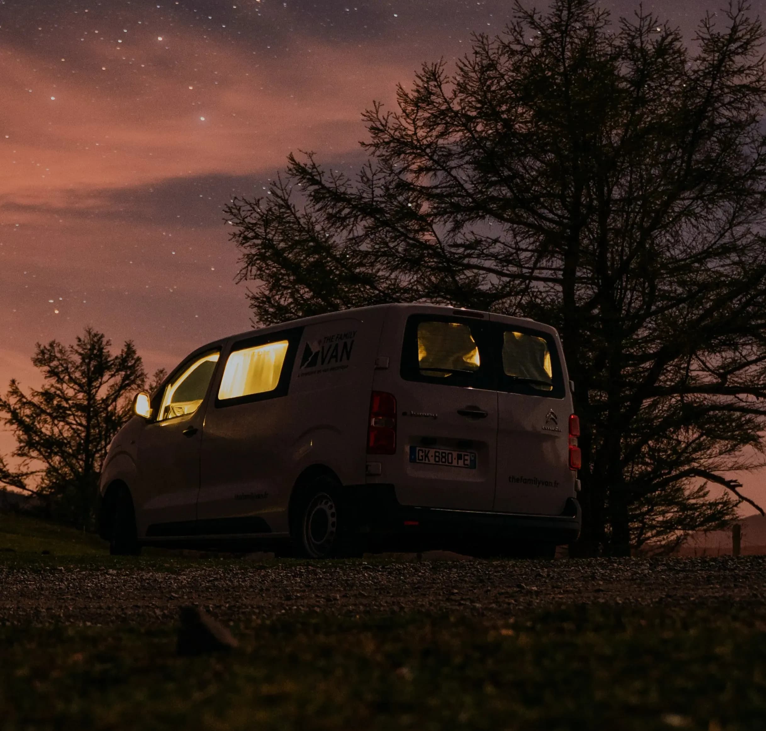 Campervan glowing from within under a starry night sky, tree silhouettes all around
